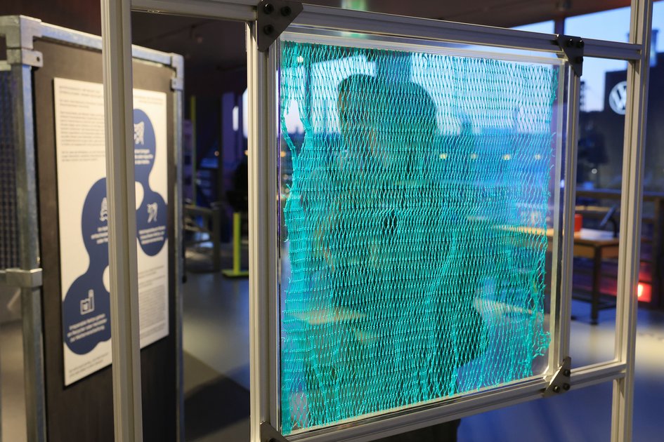 Türkises Fischernetz in einem Metallrahmen als Ausstellungsobjekt zu langlebigen Kunststoffmaterialien.