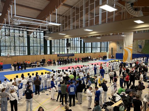 Blick in eine große Sporthalle während der Deutschen Hochschulmeisterschaft im Judo: zahlreiche Judoka stehen um die Wettkampfmatten, Offizielle bereiten die Eröffnung vor. (öffnet Vergrößerung des Bildes)