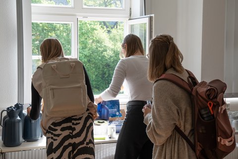 Three visitors, who can be seen from behind, are enjoying drinks and snacks at a buffet. (opens enlarged image)