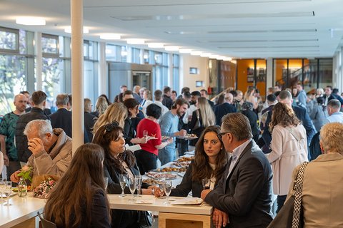 Zahlreiche Gäste beim Sektempfang im Glasgang neben der Cafeteria. Einige bedienen sich gerade am Buffet. (öffnet Vergrößerung des Bildes)