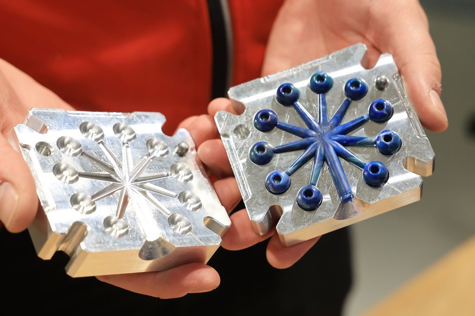 Hände halten zwei transparente Formstücke mit sternförmigen Kunststoffelementen in Silber und Blau.