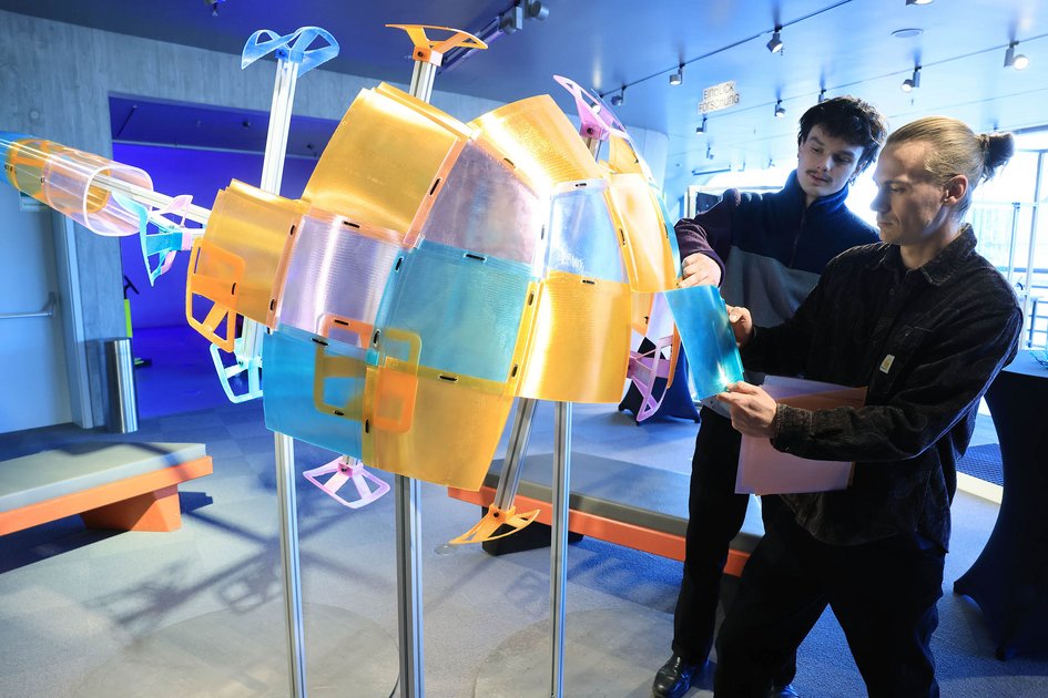 Zwei Personen betrachten und bewegen ein farbiges, aus 3D-gedruckten Kunststoffelementen zusammengesetztes Objekt im phaeno Science Center.