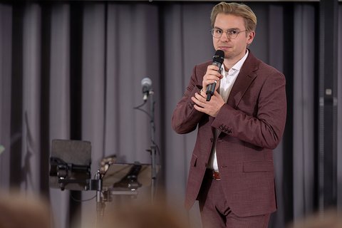 Conrad Wegmann im brauen Anzug mit weißem Hemd bei seinem Alumni-Grußwort. (öffnet Vergrößerung des Bildes)
