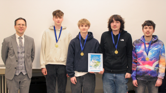 Gruppenbild von links nach rechts: Prof. Dr. Henning Zindler und vier Schüler der Sekundarstufe 2 der Wilhelm-Bracke-Gesamtschule stehen nebeneinander. Die Schüler tragen jeweils eine Medaille und halten in der Mitte das Preisgeld in einem Bilderrahmen.