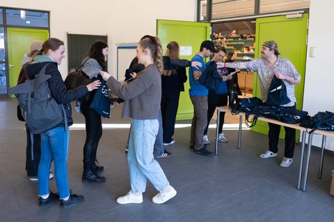 Tutor:innen stehen vor der Tür zum Hörsaal und geben Ostfaliataschen zur Begrüßung an die ankommenden Erstsemester aus. (öffnet Vergrößerung des Bildes)