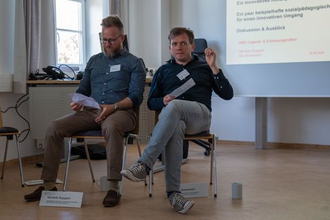 Henrik Ruppert and Nils Borkowski sit together on two chairs and explain their workshop to the group. (opens enlarged image)