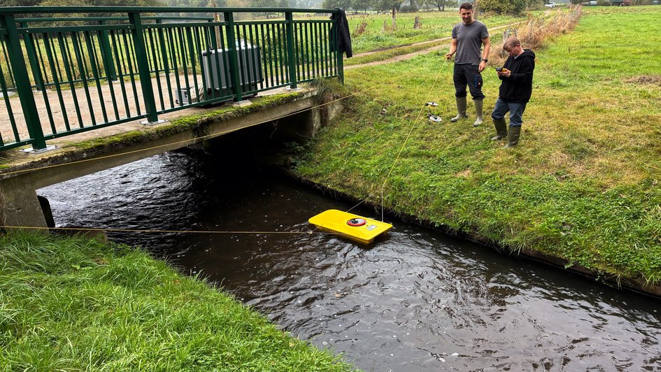 Jasper Seng (links im Bild) und Olaf Baalhorn (rechts im Bild) führen gemeinsam eine Durchflussmessung durch. Während sie das ADCP-Messgerät im Wasser positionieren, überprüfen und steuern sie die Messung über das angeschlossene Bedienteil. Foto: Marie Ruhm/Ostfalia