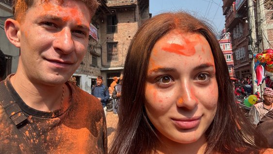 Niklas Wilms und Gökcen Sungur beim Neujahrfest in Nepal lächeln in die Kamera. Sie haben orangene Farbspritzer im Gesicht und auf der Oberbekleidung.
