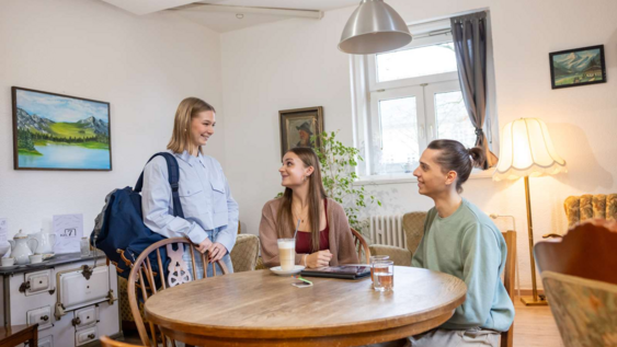 3 Studierende sitzen zusammen am Tisch und unterhalten sich