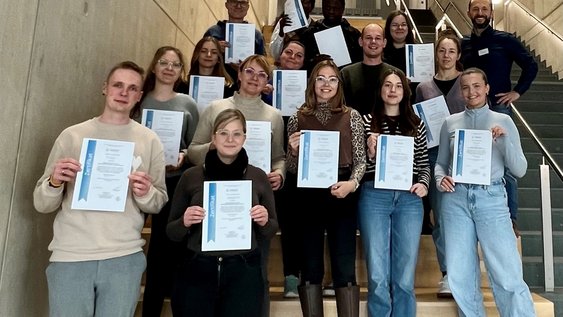 Die Seminar-Teilnehmenden mit ihren Bescheinigungen auf der Treppe im Fakultätsgebäude G