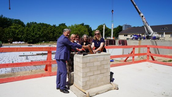 Wolfenbüttels Erster Stadtrat Thorsten Drahn, Dr. Sandra Roddewig vom Niedersächsischen Ministerium für Wissenschaft und Kultur, Architektin Maria Pfitzner, Anke Westphal vom Staatlichen Baumanagement und Ostfalia-Präsidentin Prof. Julia Siegmüller beim Versenken der Zeitkapsel an der Baustelle der neuen Sporthalle.
