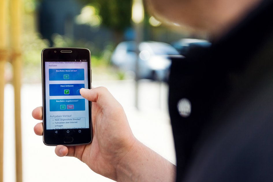 Eine Hand hält ein Handy. Auf dessen Display ist eine Checkliste zum Fahren mit öffentlichen Verkehrsmitteln zu lesen