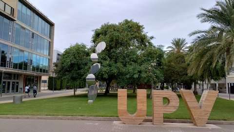 Vor einer Rasenfläche mit zahlreichen Bäumen stehen die hölzernen Buchstaben UVP. Links befindet sich ein Universitätsgebäude. (öffnet Vergrößerung des Bildes)