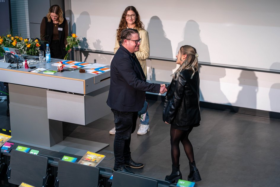 Dozent gratuliert Studentin im Rahmen einer Ehrung. 