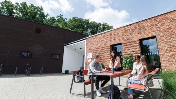 Eine Gruppe Studierender sitzt vor dem Hochschulgebäude in Suderburg