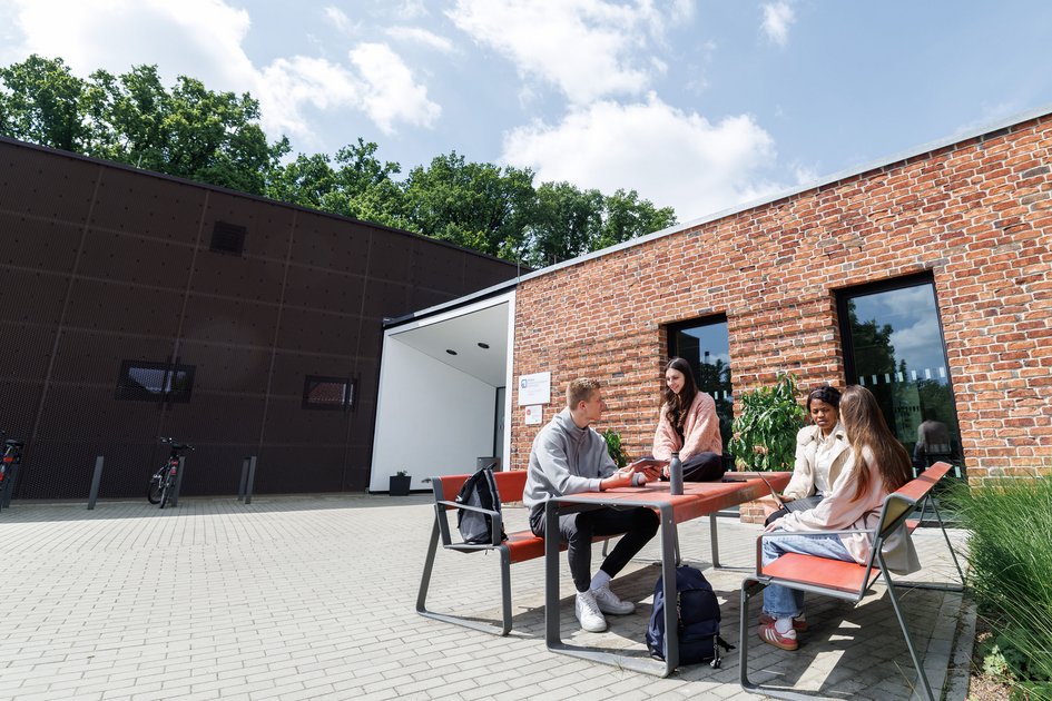 Eine Gruppe Studierender sitzt vor dem Hochschulgebäude in Suderburg