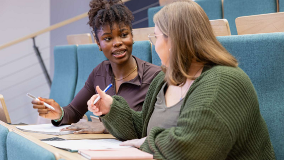2 Studierende unterhalten sich angeregt im Hörsaal