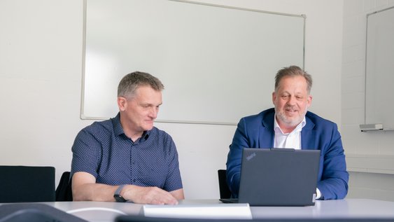 Prof. Dr.-Ing. Lars Kühl und Prof. Dr.-Ing. Jens Wagner besprechen gemeinsam ein Forschungsprojekt an einem Besprechungstisch und blicken auf einen geöffneten Laptop.