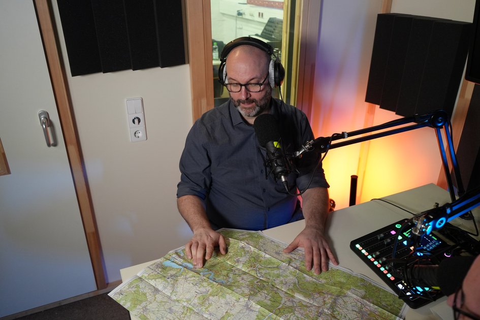 Erik Neumeyer sitzt vor einem Podcastmikrofon im Studio und spricht über Wandertourismus und nachhaltige Wegeplanung.