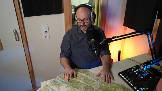 Erik Neumeyer sitzt vor einem Podcastmikrofon im Studio und spricht über Wandertourismus und nachhaltige Wegeplanung.