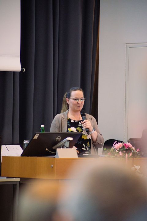 Fernaufnahme von Frau Ostermann bei ihrer Präsentation, wie ihr Weg nach dem Studium aussah bei der Absolventenfeier in der Aula der Ostfalia Hochschule (öffnet Vergrößerung des Bildes)