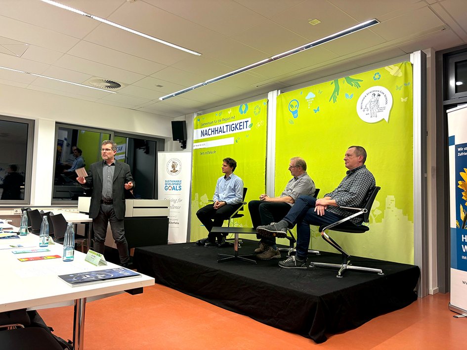 Bei der Podiumsdiskussion: Vor dem Podium links steht Prof. Dr. Litschen, auf dem Podium die Vortragenden der Veranstaltung.