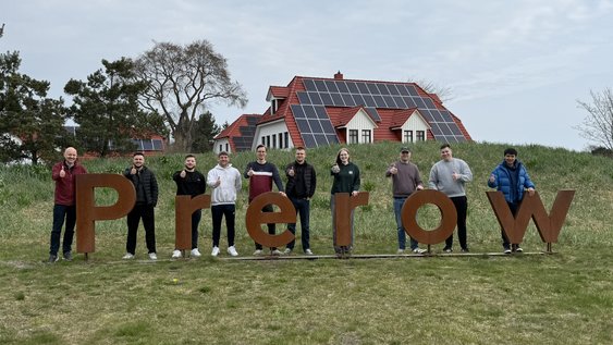Students stand in front of a sign bearing the word 'Prerow'