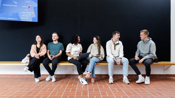 Studierende sitzen auf einer Bank im Foyer des H-Gebäudes.
