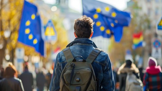 Studierender mit Rücksack von hinten inmitten einer Guppe, die Europaflaggen schwenkt