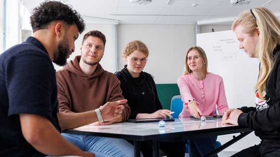 Studierende sitzen diskutierend an einem Tisch.