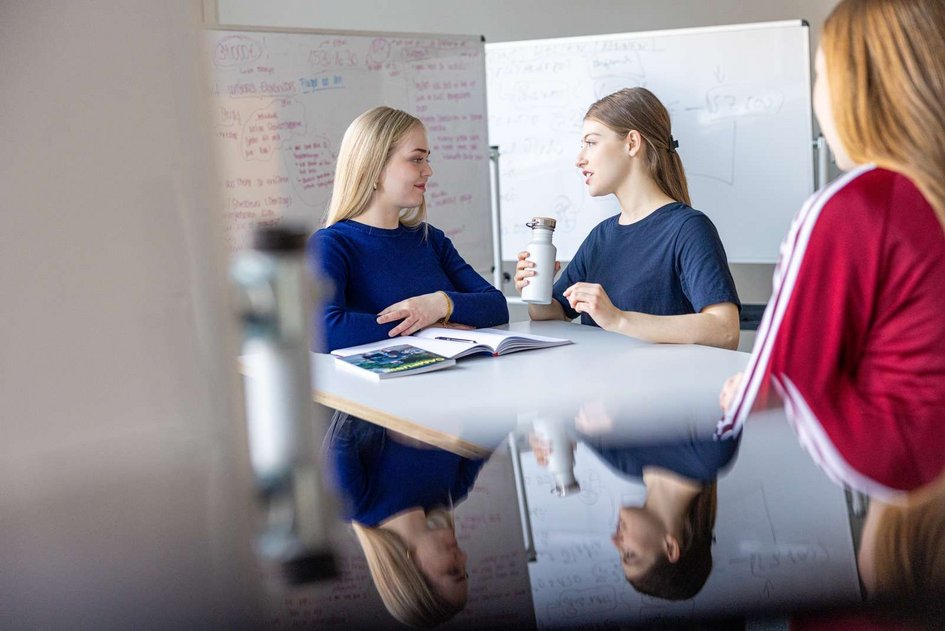Drei Frauen stehen an einem Arbeitstisch und tauschen sich aus (öffnet Vergrößerung des Bildes)