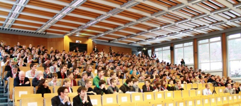 Besucherinnen und Besucher des Kongresses sitzen in den typischen Sitzreihen eines Hörsaals.