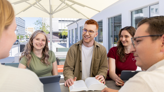 Studierende vor der Mensa an einem Stehtisch