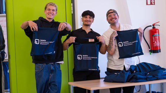 Drei Tutoren halten freudestrahlend die Begrüßngstaschen für die Erstsemester Richtung Kamera