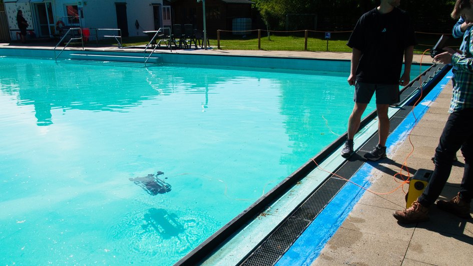 Masterstudierende üben die Stuerung einer Unterwasserdrohne in einem Schwimmbad.