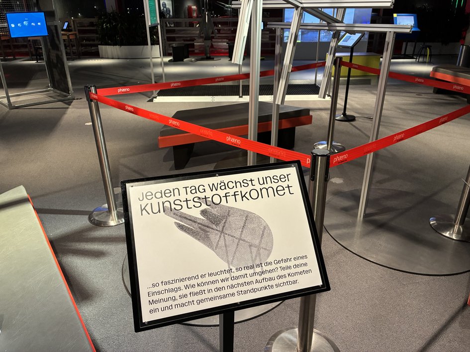 Hinweisschild mit der Aufschrift „Jeden Tag wächst unser Kunststoffkomet“ vor der Installation im phaeno.
