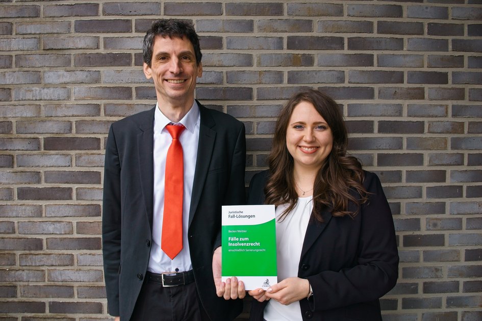 Prof. Dr. Udo Wolfgang Becker und Isabel Weibler halten ihr Lehrbuch "Fälle zum Insolvenzrecht" in den Händen.