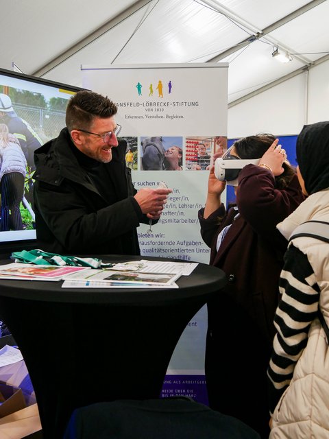 Am Info-Stand wird eine VR-Brille getestet. Beide Personen sind begeistert.