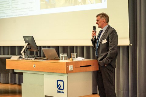 Aufnahme von Prof. Dr.-Ing. Lars Kühl auf der Bühne in der Aula der Ostfalia Hochschule und hält ein Mikrofon in der Hand. (öffnet Vergrößerung des Bildes)
