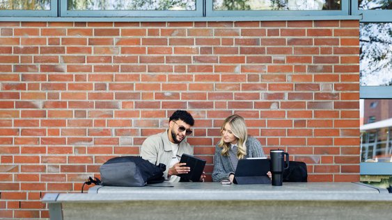 Studierende sitzen draußen und lernen am Tablet.