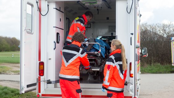 zwei Notfallsanitäter und eine Notfallsanitäterin mit Patienten im und am Rettungswagen