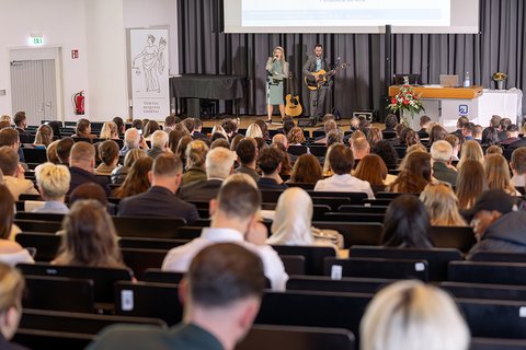 Blick von hinten über das Auditorium auf die Bühne auf der das Musikduo "Perceived as One" steht. (öffnet Vergrößerung des Bildes)