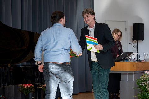 Prof. Dr. Jürgen Boeckh übergibt einem Absolventen auf der Bühne seine Urkunde und schüttelt dabei seine Hand. (öffnet Vergrößerung des Bildes)