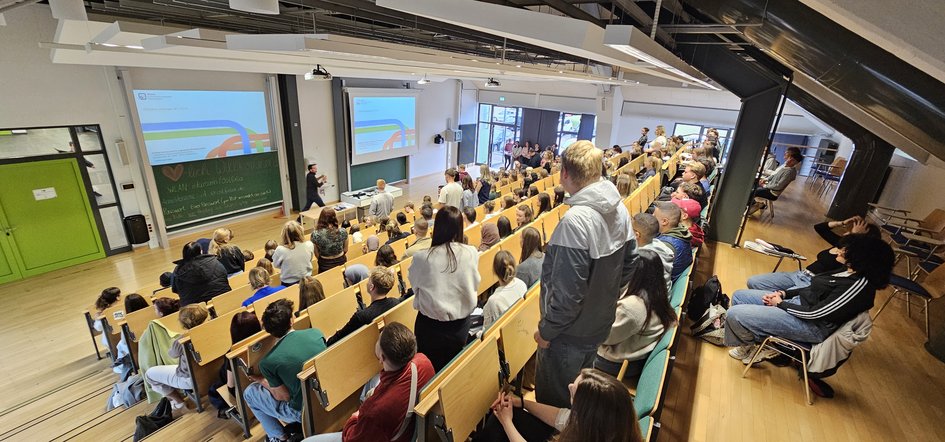 Der Hörsaal Am Exer 11 gefüllt mit Erstsemestern mit Blick auf die Tafel an der Helge Keller alle Anwesenden begrüßt.