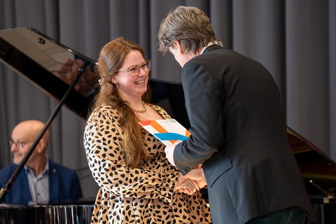 Prof. Dr. Jürgen Boeckh übergibt einer Absolventin auf der Bühne ihre Urkunde und schüttelt dabei ihre Hand. (öffnet Vergrößerung des Bildes)