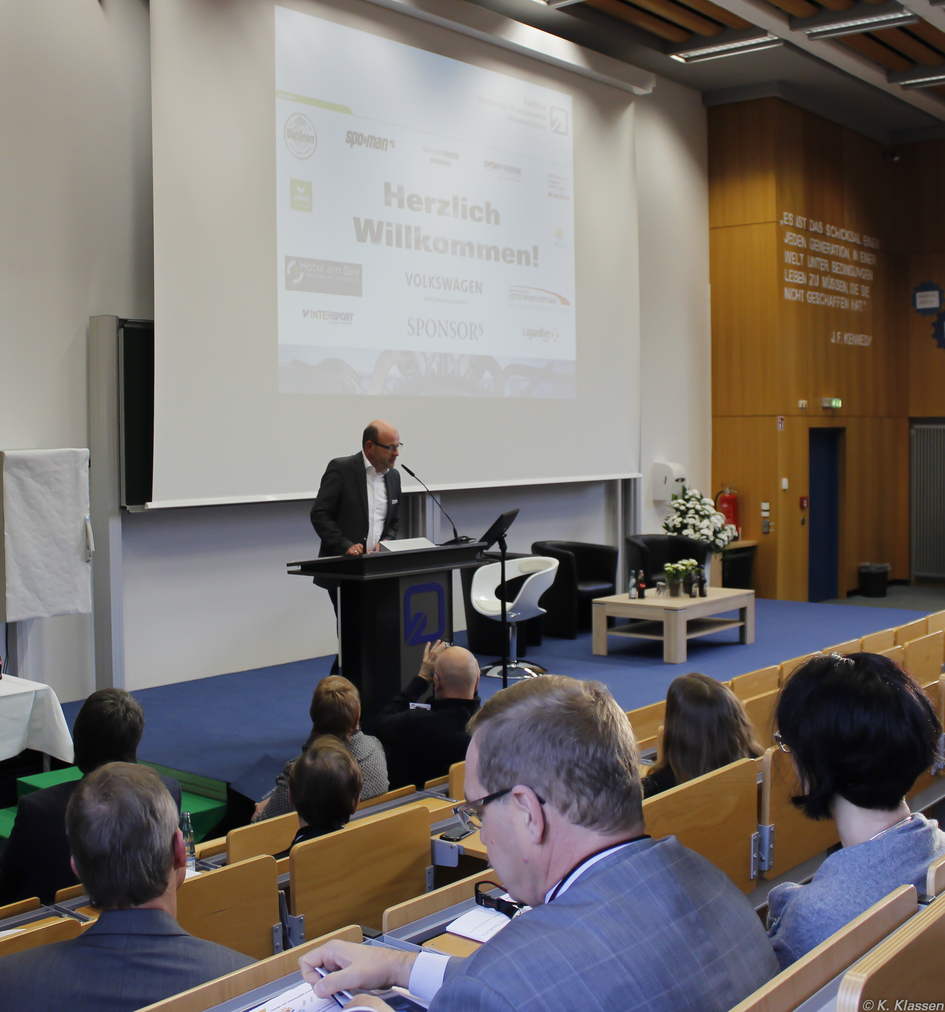 Der Dekan steht am Rednerpult auf der Bühne und eröffnet den Kongress.