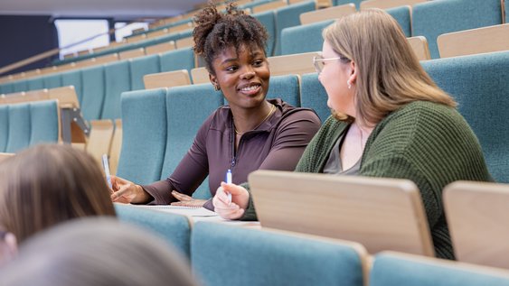 Two female students are sitting in the lecture theatre, chatting