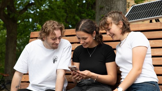 Studierende schauen gemeinsam auf ein Smartphone und schauen sich die Facebookseite der Fakultät Versorgungstechnik an. 