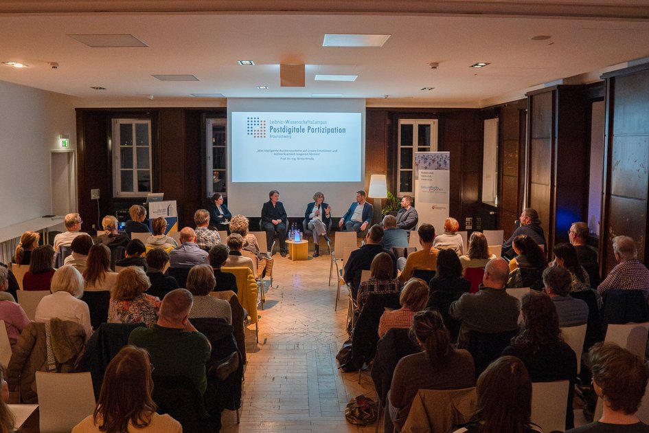 Blick von Hinten auf den vollen Saal und die Podiumsdiskussion.