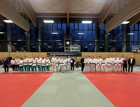 Drei Judo-Teams stehen in einer Sporthalle nebeneinander zur Siegerehrung der Deutschen Hochschulmeisterschaft, begleitet von Offiziellen am Mattenrand. (öffnet Vergrößerung des Bildes)
